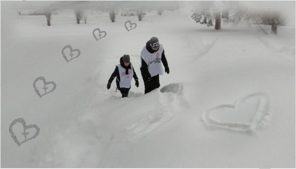 Kaksi yhteisvastuu-liiviin pukeutunutta kiipeää lumivuorelle. Taustahangella yhteisvastuu-logon sydämiä.