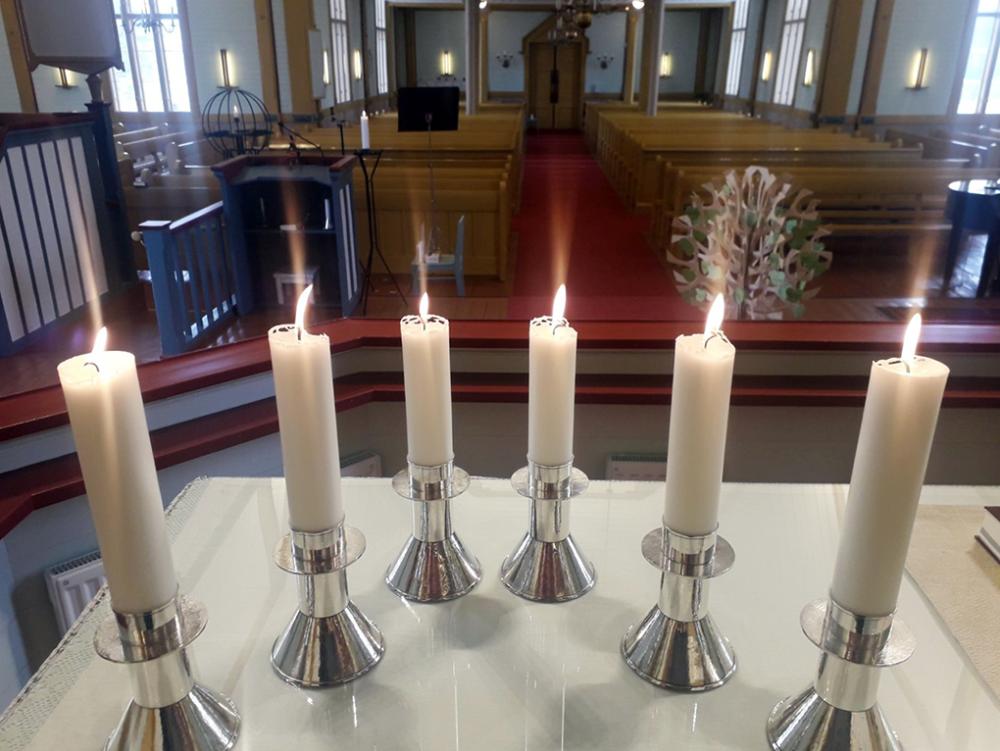 Kuusi kynttilää palaa kirkossa alttarilla ja taustalla näkyy kirkkosali