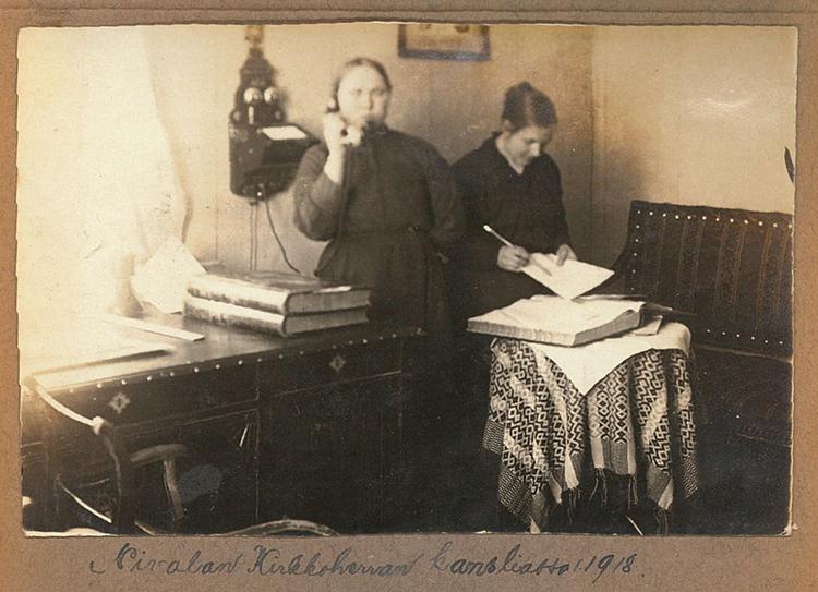 Vanha kuva kirkkoherranvirastosta vuodelta 1918, jossa nainen on puhelimessa ja toinen nainen kirjoittaa.