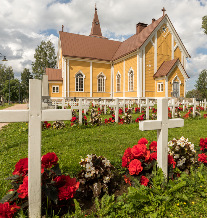 Sankarihaudat kesäkukkien loistossa, taustalla Pyhän sydämen kirkko